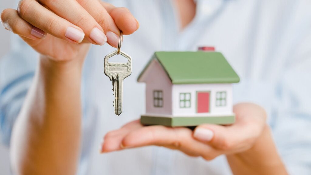 A miniature home next to a key is being held. How to prevent break-ins.